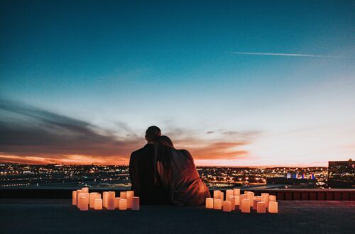 Ein Paar umarmt sich an einem romantischen Ort mit Kerzenlicht und blickt gemeinsam auf eine Stadt bei Sonnenuntergang, um ihre Papierhochzeit zu feiern